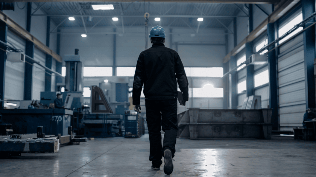 Am person walking inside a factory. The factory has a darker theme
