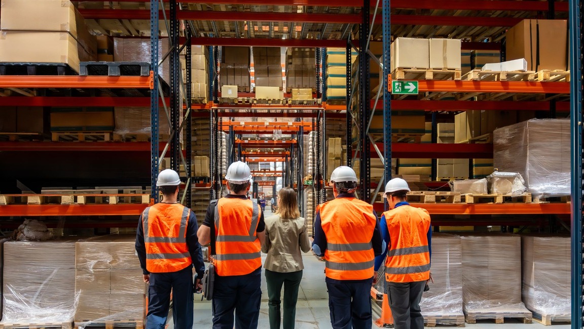 Manufacturing and quality team walking a warehouse aisle of palletised finished goods during a batch traceability review